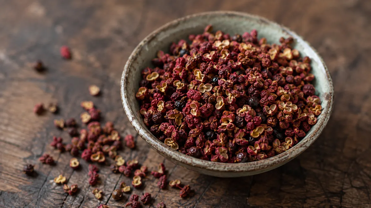 Dried red Sichuan peppercorns in a small ceramic bowl on a worn wooden surface