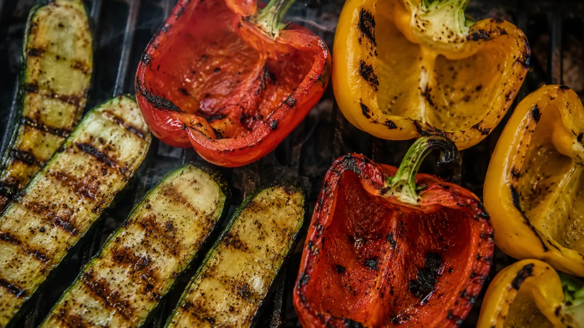 Close-up of bell peppers and zucchini charring on iron grill grates