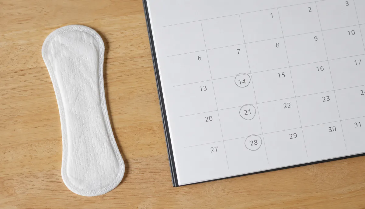 Close-up of a calendar marked with cycle dates next to a small panty liner, representing early pregnancy spotting