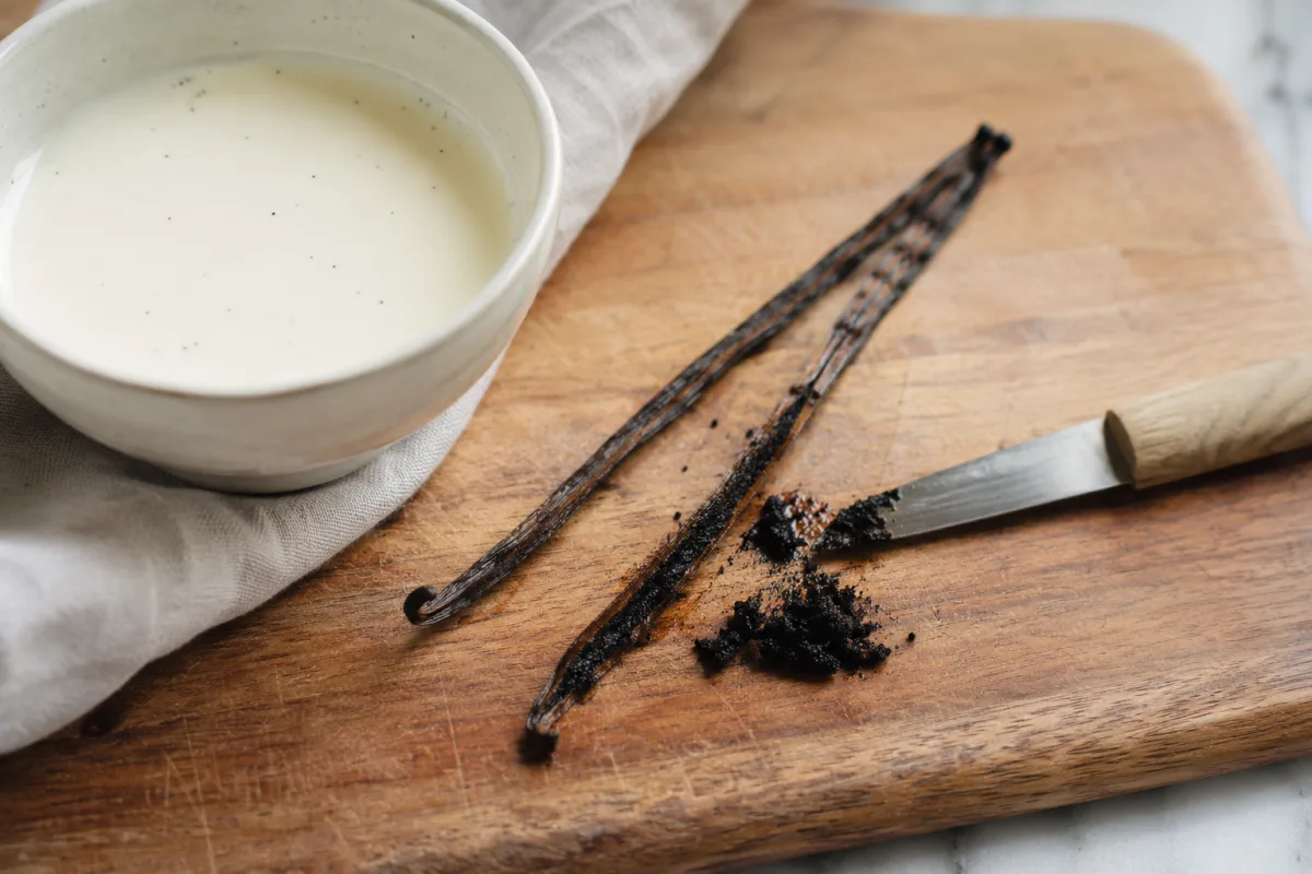 Vanilla bean being split and scraped on a cutting board